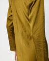 Close-up of a person wearing a long-sleeved olive yellow satin or silk dress, showing the fabric's sheen and drape against a plain white background.