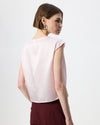 A woman shown from the back wearing a light pink sleeveless top and burgundy trousers, photographed against a clean white studio background.