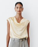 Woman wearing a light yellow sleeveless top and gray pants against a white background