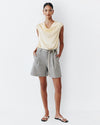 Woman wearing a light-colored sleeveless top and gray shorts on a white background