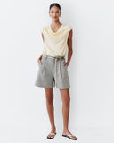 Woman wearing a light yellow sleeveless top and gray shorts on a white background