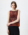 A model wearing a sleeveless top with an abstract, textured pattern in shades of rust, brown, and burgundy, paired with black trousers, against a plain light gray background.