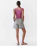 Woman wearing a pink tank top and grey shorts on a white background