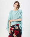 A model wearing a light blue draped top and a dark floral skirt against a plain white studio background.