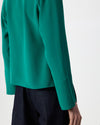 Close-up of a person wearing a long-sleeve emerald green blouse with dark navy pants against a clean white studio background.