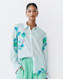 Woman wearing a striped shirt with colourful Sama Print designs and green pants on a light background