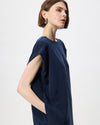 A woman wearing a loose, short-sleeve navy blue dress, shown in profile against a clean light gray studio background.