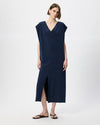 A woman modeling a navy blue midi dress with a V-neckline, cap sleeves, and a front slit, paired with black flip-flop sandals against a light gray studio background.