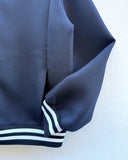 Close-up of a navy blue textured jacket sleeve with white and navy striped ribbed cuffs, shown against a plain off-white background.
