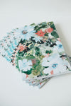 A stack of rectangular paper notebooks, featuring a colourful watercolor floral pattern with white, blue, pink, and green flowers on a white background.