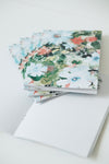A stack of floral-patterned notepads with white lined pages, arranged on a clean white surface.