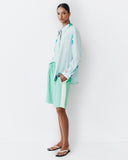 Model wears teal shorts with light lemon yellow racing stripe down the sides of the shorts.