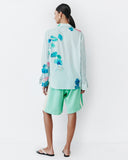 Model wears teal shorts with light lemon yellow racing stripe down the sides of the shorts.