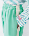 Model wears teal shorts with light lemon yellow racing stripe down the sides of the shorts.
