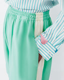 Model wears teal shorts with light lemon yellow racing stripe down the sides of the shorts.