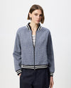 A woman modeling a navy blue bomber jacket with a floral pattern, black and white striped ribbed collar, cuffs, and hem, paired with dark trousers against a light gray studio background.