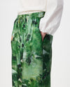 Green abstract patterned wide-leg trousers with an elastic waistband, shown on a model wearing a white textured blouse against a light gray background.