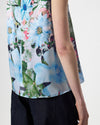 A close-up of a model wearing a sleeveless top with a vibrant blue, green, and pink floral print, paired with dark navy pants against a light gray background.