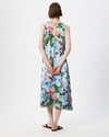 A woman viewed from behind wearing a sleeveless midi dress with a colorful floral print in green, blue, pink, and white, paired with black flip-flop sandals, against a plain white studio background.
