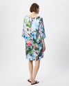 A woman viewed from the back wearing a knee-length floral dress with wide three-quarter sleeves. The dress has a multicolor print featuring blue, pink, green, and white tones.