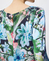 A close-up of a long-sleeve blouse with a vibrant watercolor floral print, featuring light blue, green, pink, and white flowers on a dark background, shown on a mannequin.