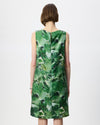 A woman viewed from the back wearing a sleeveless knee-length dress with an abstract green and white watercolor-style print, set against a plain light gray studio background.