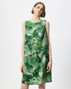 A woman modeling a sleeveless knee-length dress with an abstract green and white watercolor-style print, paired with black flip-flop sandals against a plain light gray studio background.