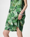 A close-up of a model wearing a green abstract print dress with a silver cuff bracelet, set against a plain light gray background.