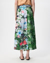 A model is shown from the back wearing a high-waisted midi skirt with a vibrant watercolor floral and botanical print. The skirt features shades of green, blue, pink, and white.