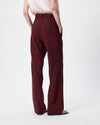 A person shown from the back wearing high-waisted, wide-leg trousers in a deep burgundy color, paired with a pale pink top and black sandals, against a plain white studio background.