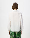 A model viewed from the back wearing a white long-sleeve textured blouse and green patterned trousers, set against a plain white studio background.