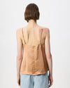 A woman shown from the back wearing a light brown linen camisole top with thin straps and light blue denim pants, set against a plain white studio background.