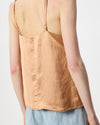 A close-up back view of a model wearing a light peach-beige linen camisole top with thin straps and a light blue denim skirt against a plain white background.