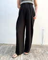 Person wearing black wide-leg pants against a white wall.