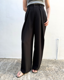 Person wearing black wide-leg pants against a white wall.
