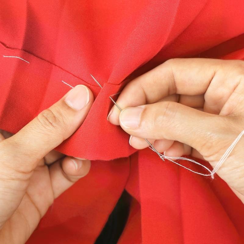 person hand sewing red fabric hem with needle