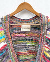 multicoloured handknitted cardigan hanging on white wall