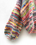 multicoloured handknitted cardigan hanging on white wall