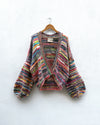 multicoloured handknitted cardigan hanging on white wall