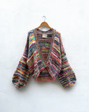 multicoloured handknitted cardigan hanging on white wall
