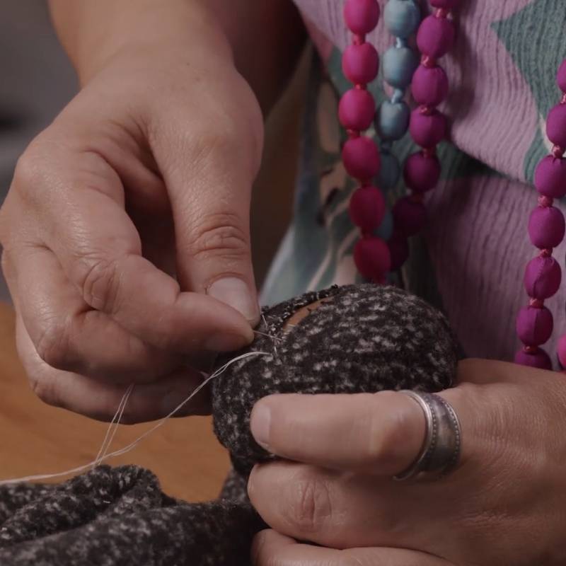 person wearing pink dress and pink necklaces hand sewing and darning a tear in a garment using a darning mushroom