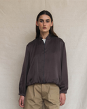 Person wearing a dark brown jacket and beige pants against a neutral background