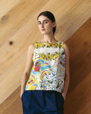 Model wearing a colorful sleeveless top with a floral and abstract design against a wooden background