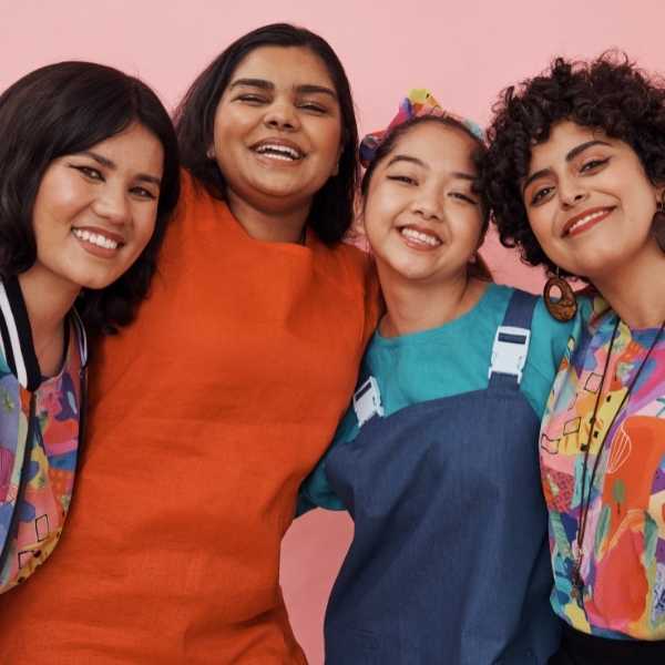four young women standing side by side smiling at the camera wearing colourful clothing