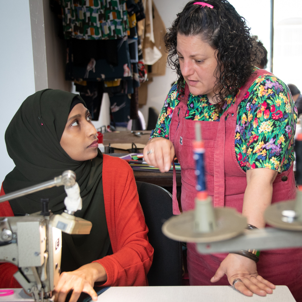 our production manager joss helping a lady sew during one of our sewing program classes