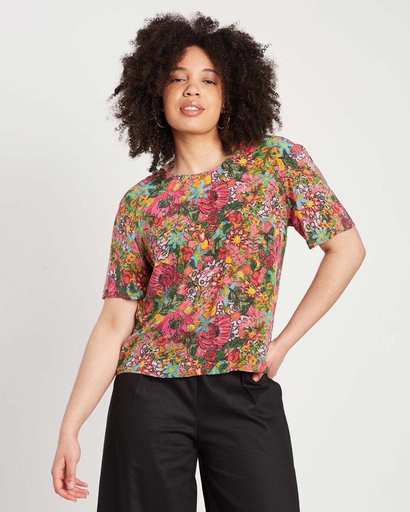 woman with curly hair and hoop earrings wearing multi colour silk fairfield bloom silk tee with short sleeves and black denim culottes