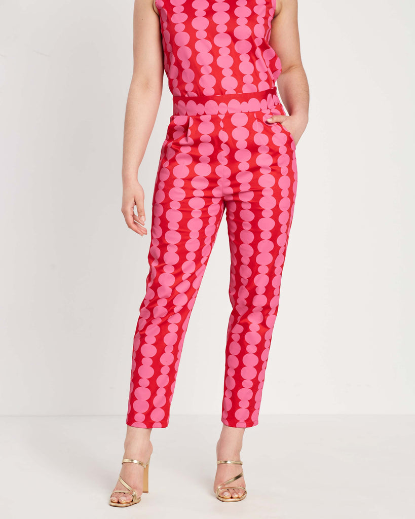 woman wearing red and pink friendship bead printed pants with hand in pocket and wearing matching co-ord top