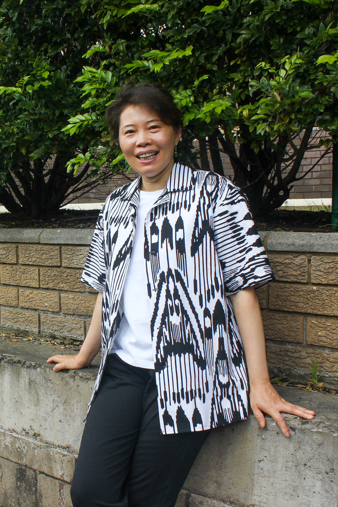 woman sitting on ledge smiling at the camera wearing short sleeve shirt with black and white print on top of a white t-shirt and black sweatpants