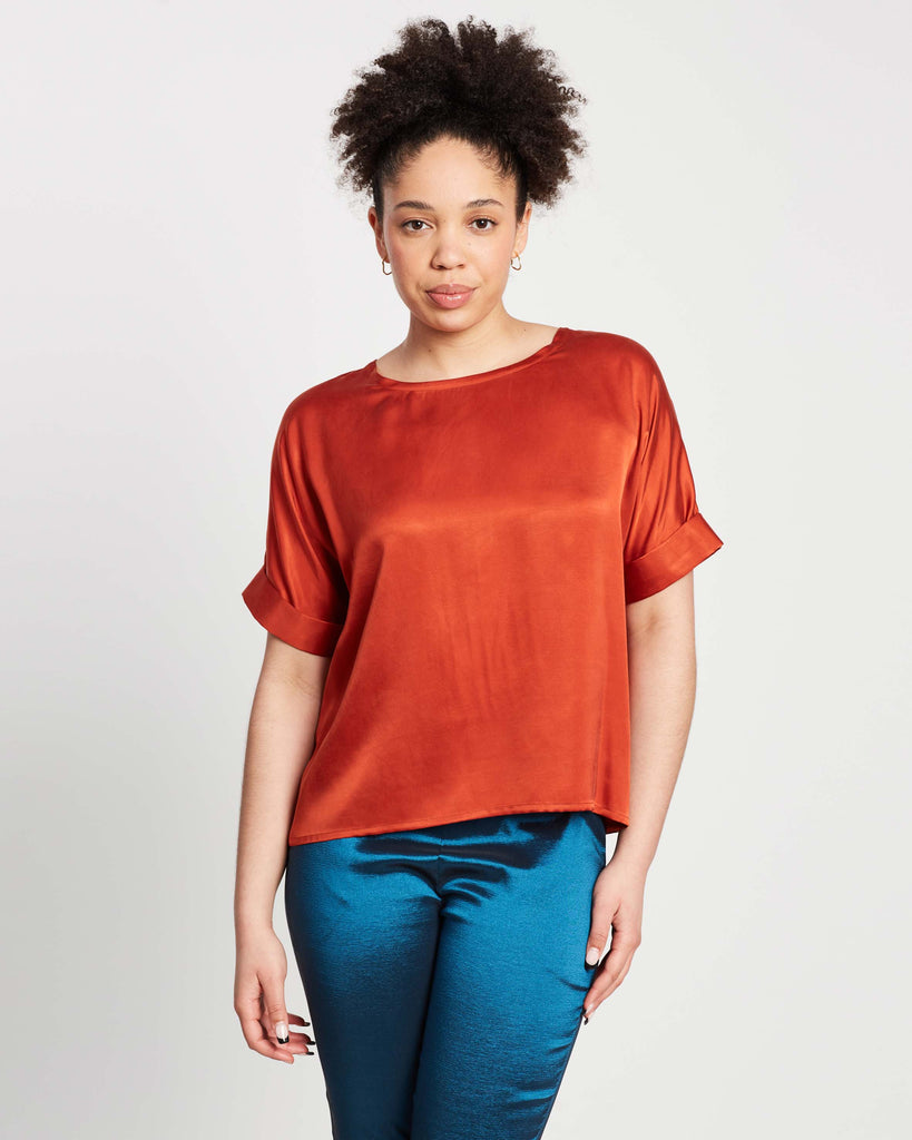 woman wearing blood orange scoop top with wide neckline and cuffed sleeves on top of teal pants