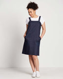 woman wears a dark indigo denim pinafore with silver buckles on top of a white t-shirt with rolled sleeves and white low sneakers